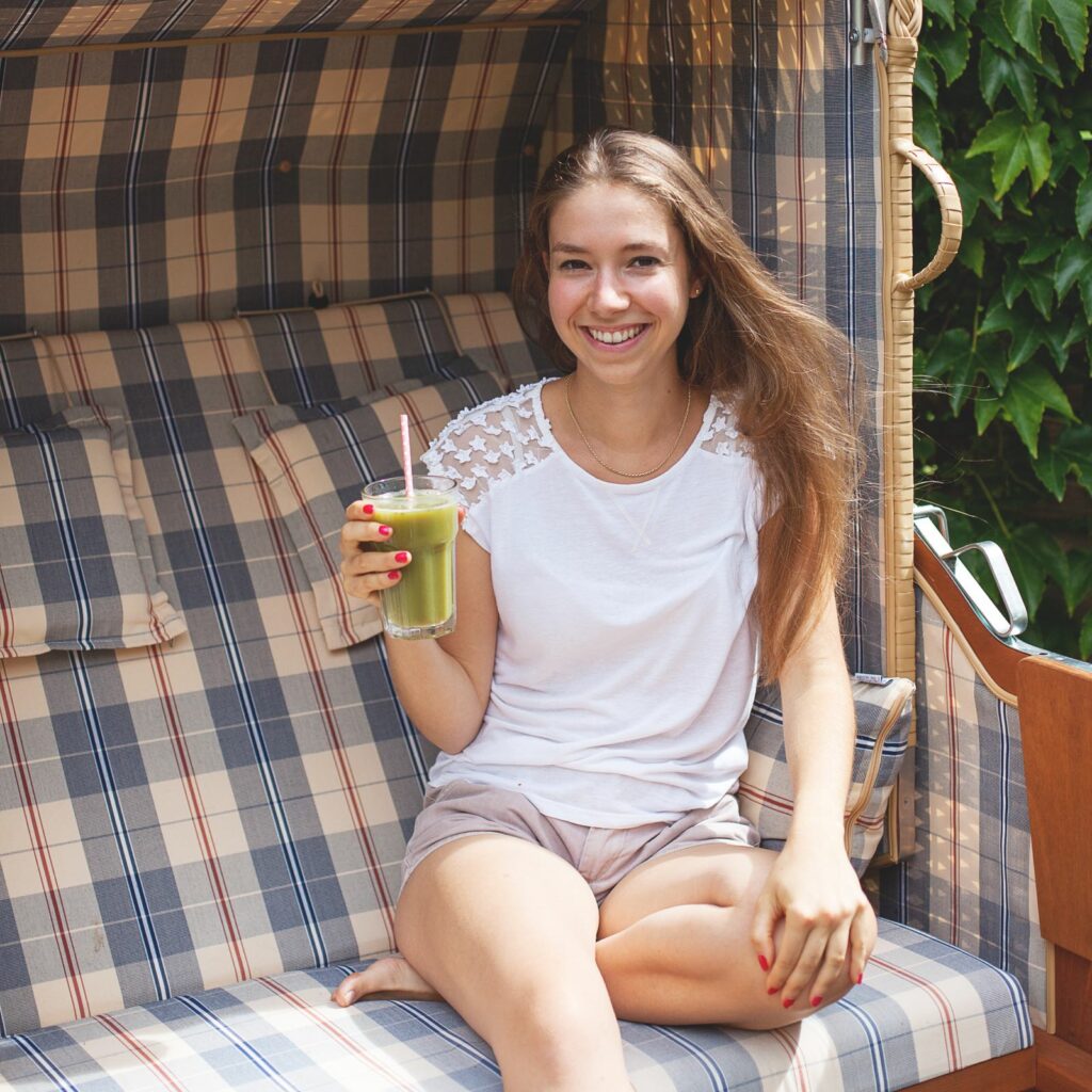 Katharina Döricht sitzt in einem Strandkorb, hält ein Glas mit grünem Saft in der Hand.