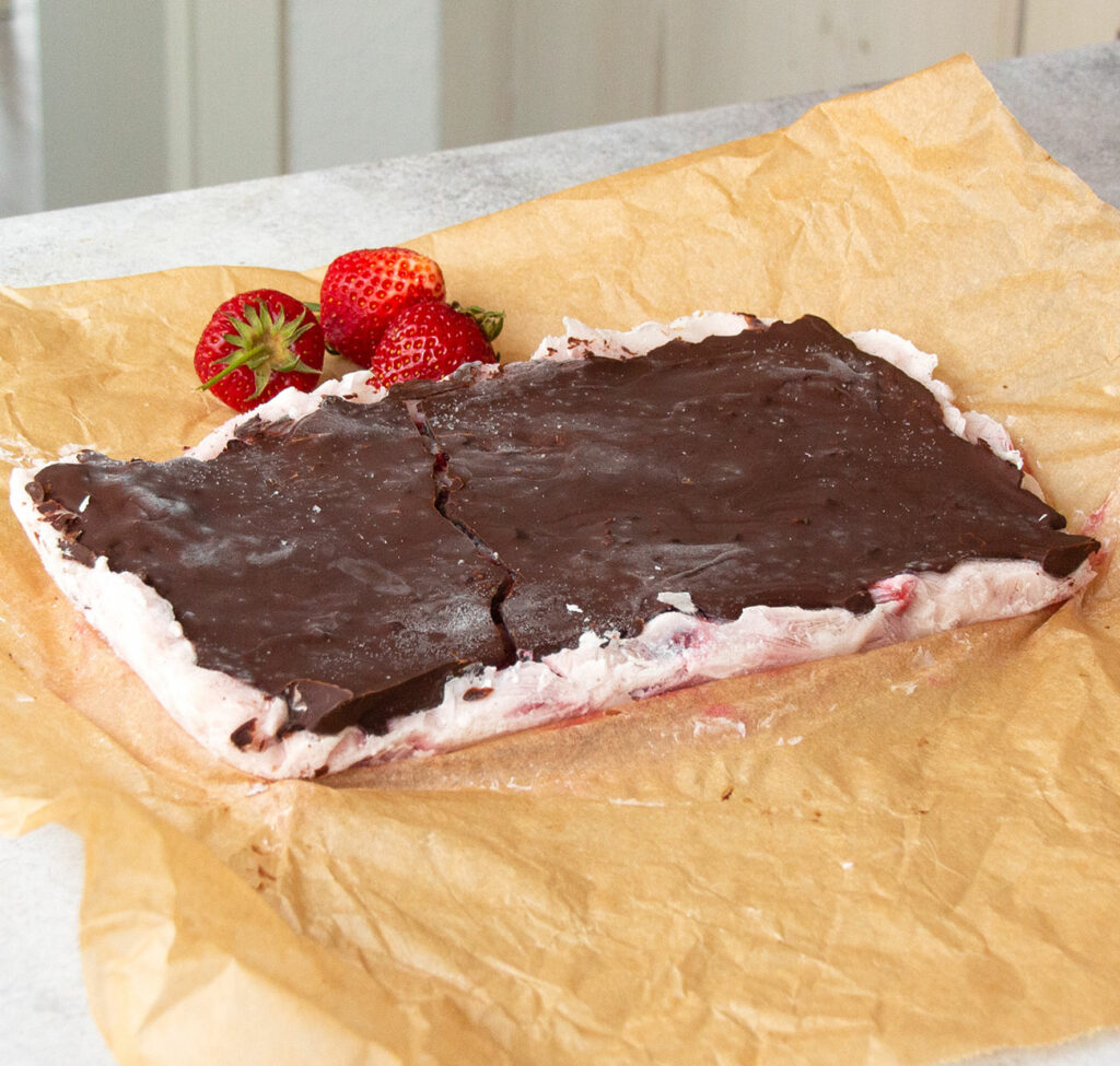 Erdbeer-Joghurt-Schokolade auf einem Backpapier. Erdbeeren liegen zur Deko dahinter.