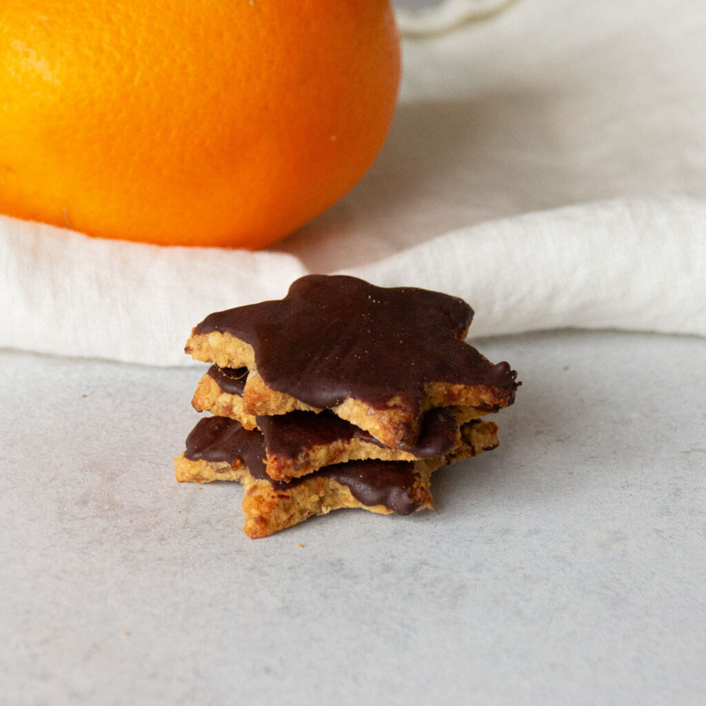 Gesunde Orangen-Plätzchen sind übereinander gestapelt. Eine Orange ist im Hintergrund.