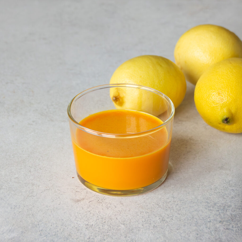 Ein Glas Ingwer-Kurkuma-Shots mit Zitronen im Hintergrund