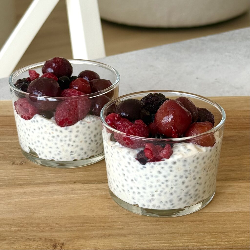 Erdnuss-Chiapudding mit Beeren in zwei Gläser auf einem braunen Brett.