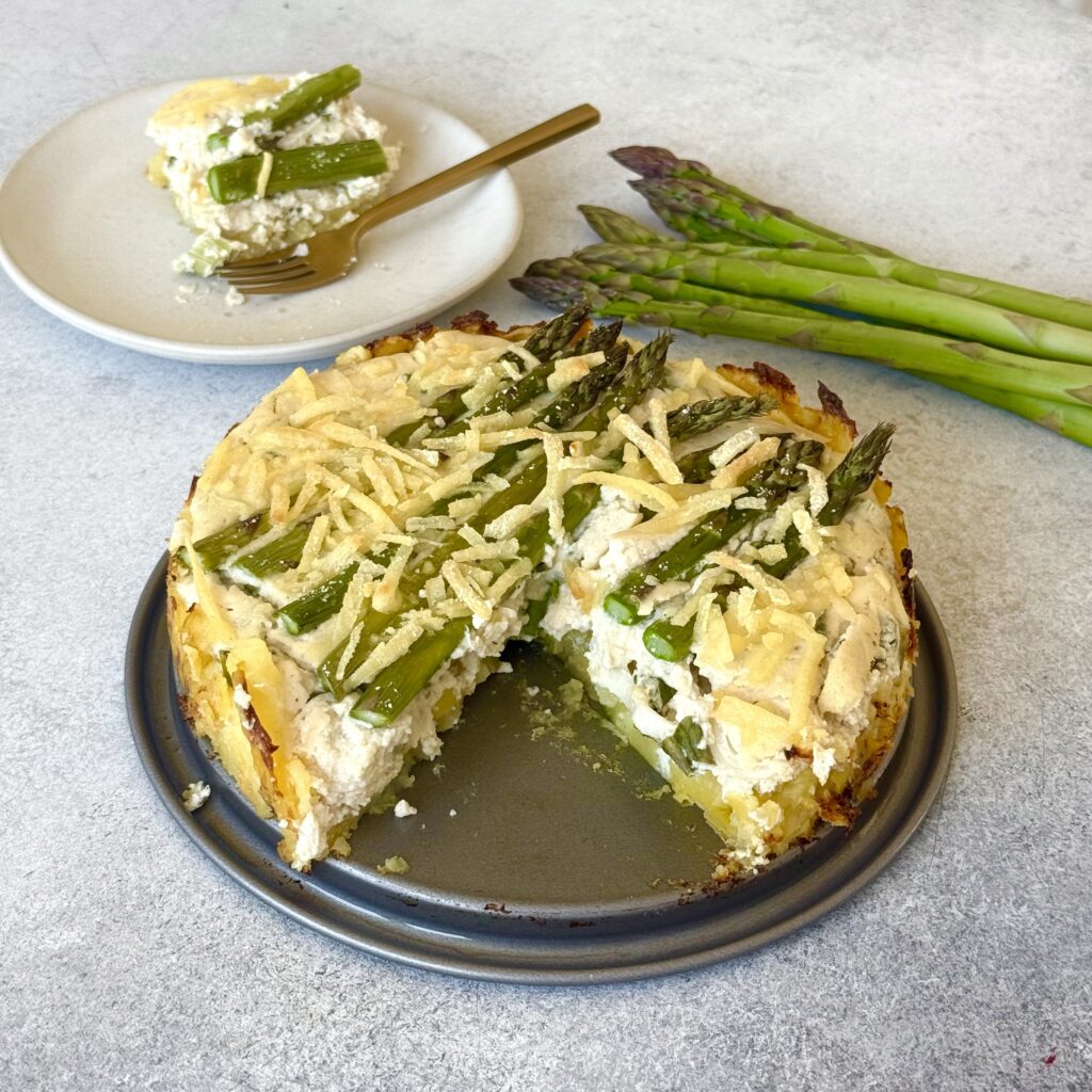 Vegane Kartoffel-Tarte mit Spargel (glutenfrei) angeschnitten mit Spargel im Hintergrund.