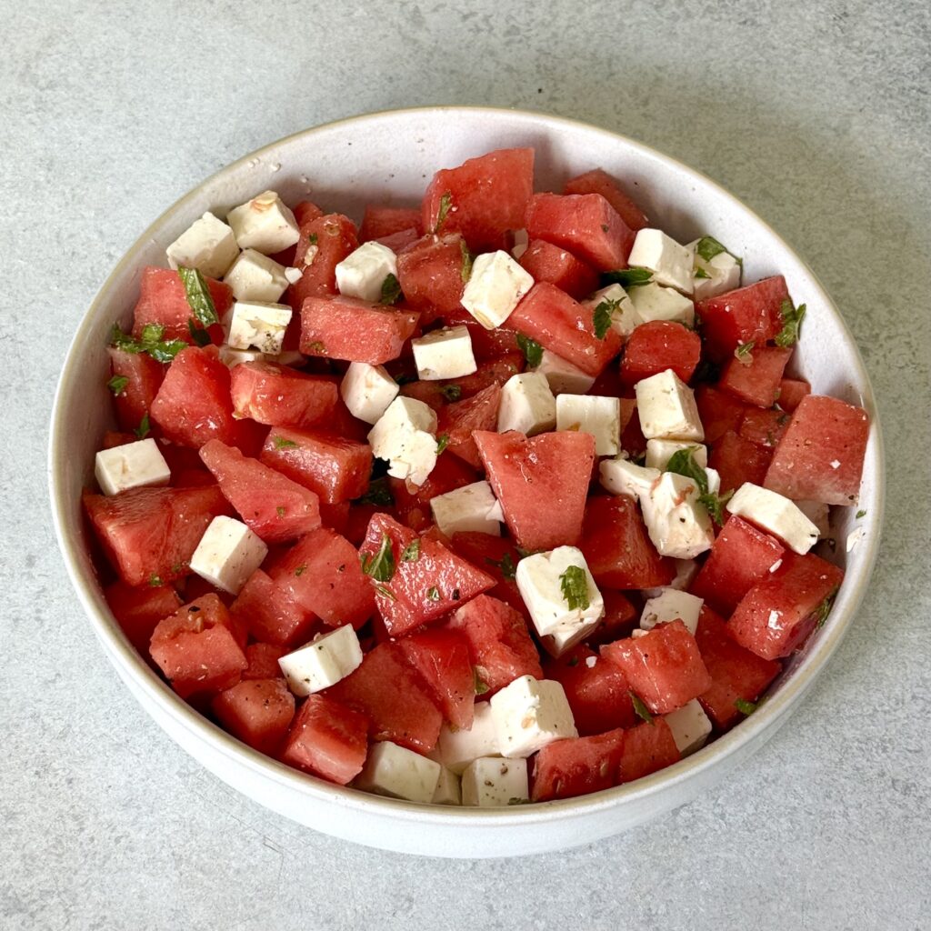 Der Wassermelonen-Feta Salat ist fertig in einer weißen Schüssel angerichtet.
