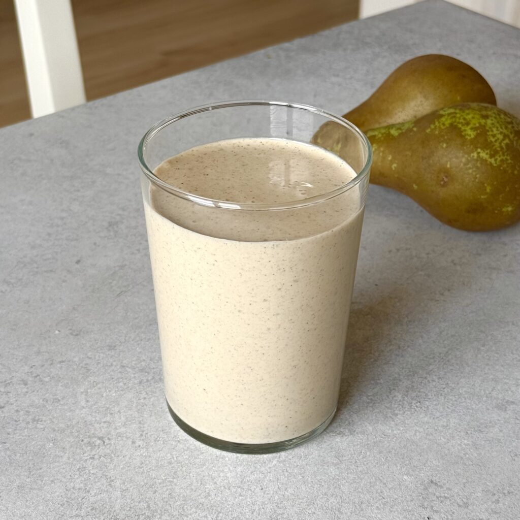 Birnen-Zimt-Protein-Smoothie (ohne Proteinpulver) in eine Glas mit zwei Birnen im Hintergrund.