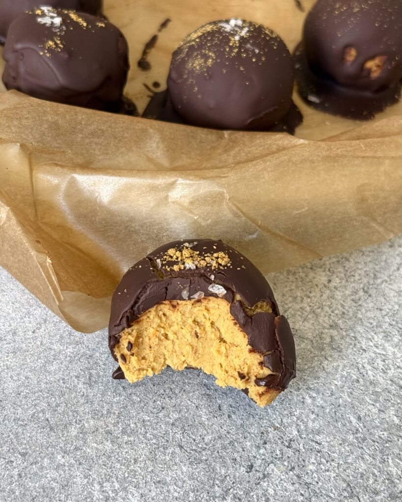 Kürbis-Protein-Bällchen mit Schokoladenüberzug angebissen zu sehen.